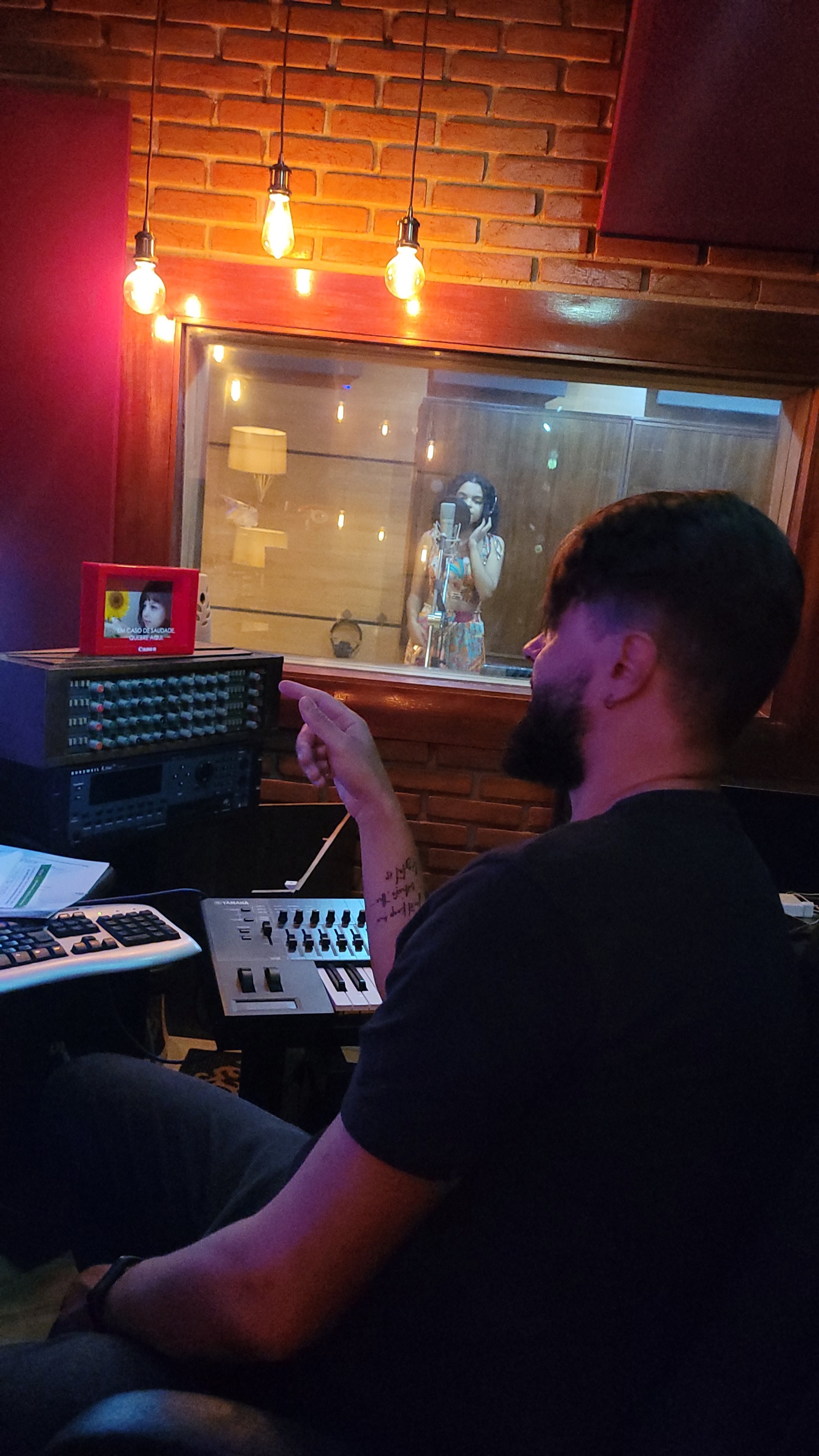 Thiago Melo dirigindo uma gravação no estúdio, com a artista na cabine